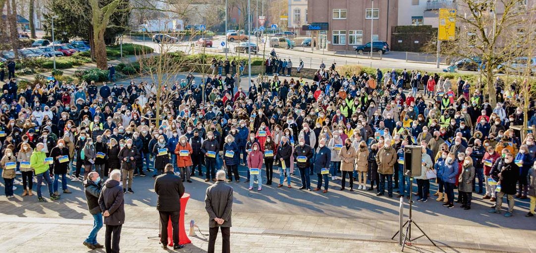 Blick aus dem Kreishaus Unna: Menschenmasse mit Ukraine Flaggen und Plakaten. Landrat Mario Löhr spricht an Stehtisch zu den Menschen. .