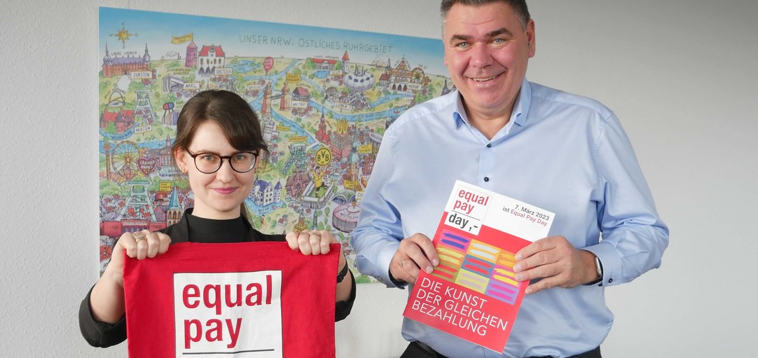 Leonie Engelhardt gemeinsam mit Landrat Mario Löhr. Sie halten eine Equal Pay Day Tasche und das EPD Magazin in die Kamera. 