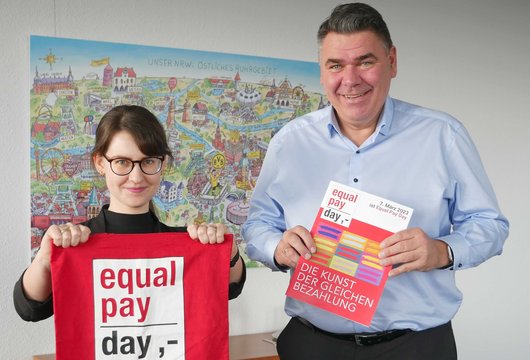 Leonie Engelhardt gemeinsam mit Landrat Mario Löhr. Sie halten eine Equal Pay Day Tasche und das EPD Magazin in die Kamera. 