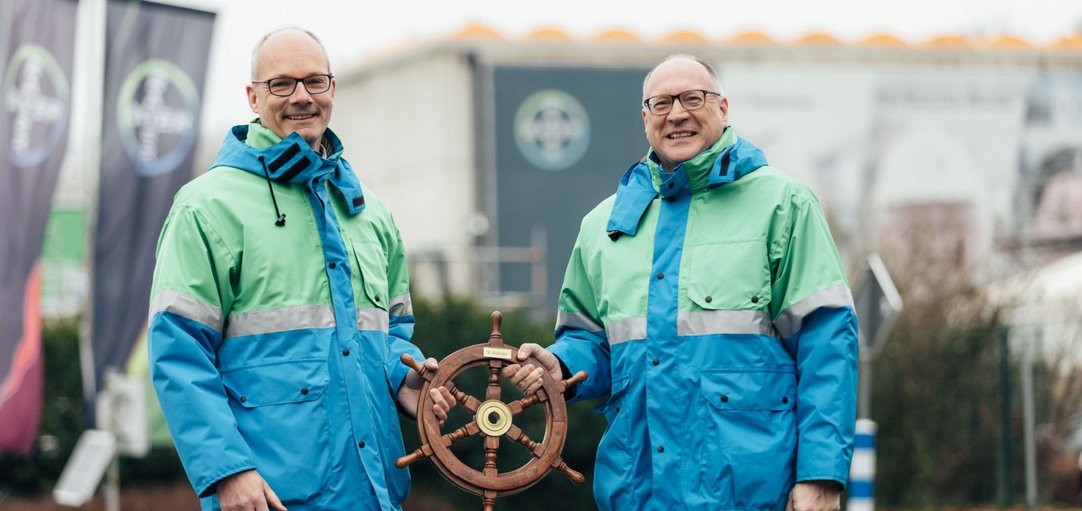 Das Bild zeigt Dieter Heinz und Thomas Wessa. Beide halten ein Steuerrad in die Kamera. 