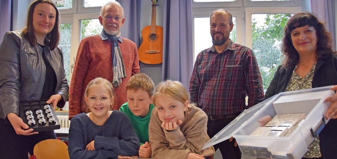 Das Bild zeigt drei Grundschulkinder mit den Mini-Robotern Ozobots. Hinter Ihnen stehen vier Erwachsene.