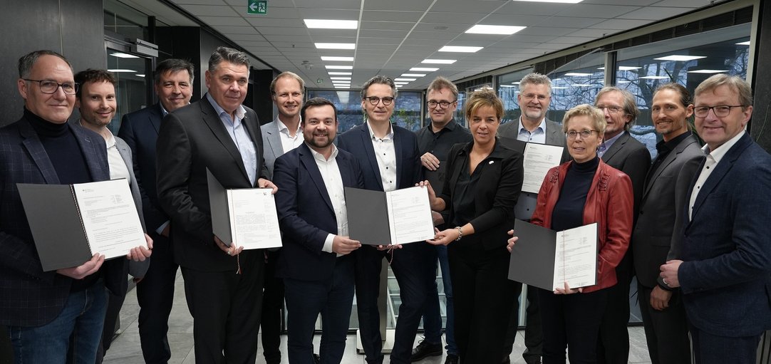 Das Bild zeigt eine Gruppe von Menschen, die einen Förderbescheid von Ministerin Mona Neubaur in Emofang nimmt,