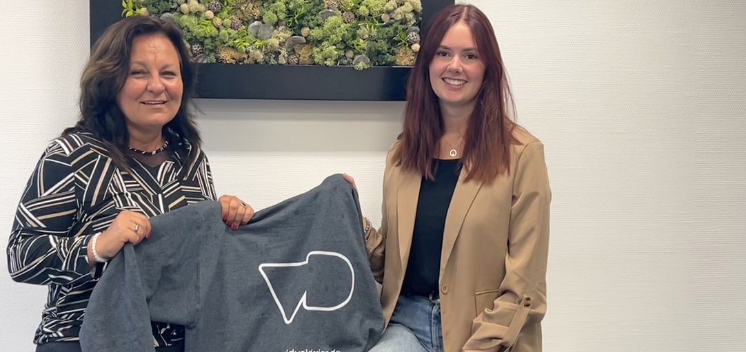 Das Bild zeigt zwei Frauen die ein Sweatshirt mit der Aufschrift Vidual Design in die Kamera halten