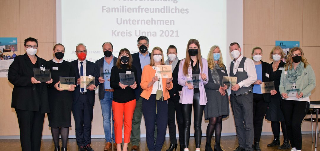 Gruppenbild der Gewinnerunternehmen mit Plaketten und Masken. 
