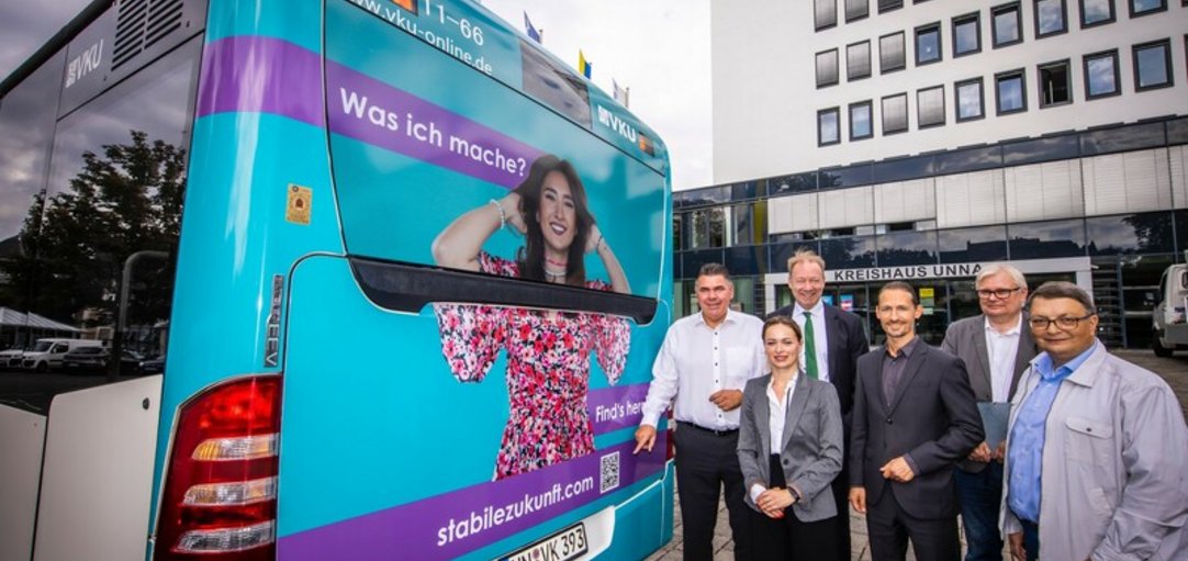 Personen vor der Rückseite eines Linienbusses. Auf dem Bus ist ein Bild der Kampagne zu sehen. 