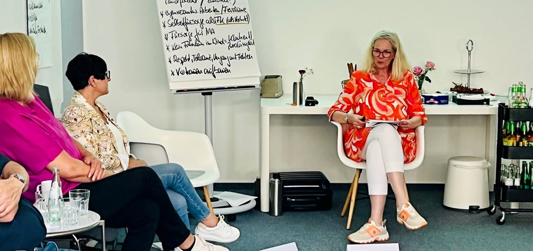 Das Bild zeigt eine Workshopsituation. Frauen und Männer sitzen im Kreis vor einer Flipchart.