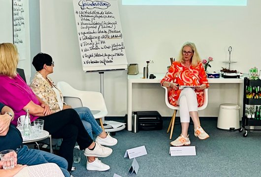 Das Bild zeigt eine Workshopsituation. Frauen und Männer sitzen im Kreis vor einer Flipchart.